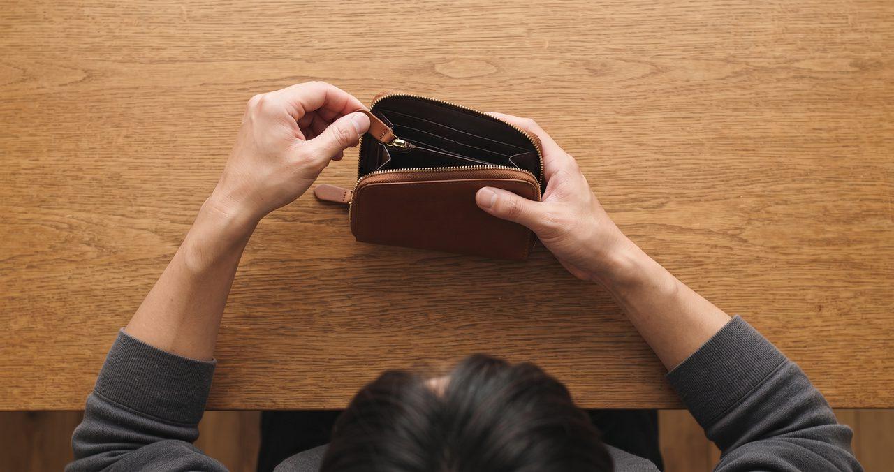 ラウンドファスナー財布を開く左手の手元、引き手の位置が見える、頭部が画面下端に見切れる俯瞰構図
